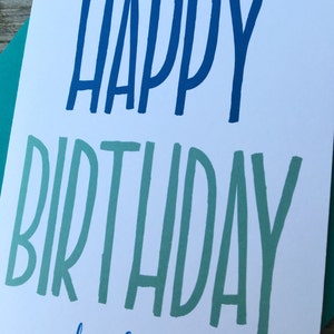 May include: A white card with blue and green lettering that says "Happy Birthday douchebag".