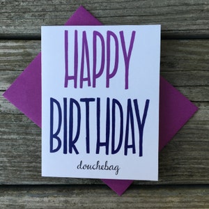 May include: A white card with a purple and blue gradient text that says "Happy Birthday douchebag". The card is sitting on a purple envelope.