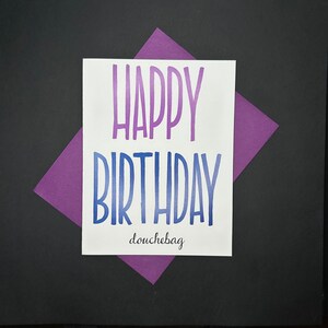 May include: A white card with the words "Happy Birthday douchebag" in blue and purple lettering.