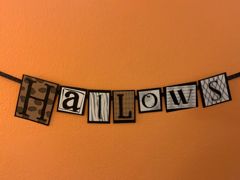 Pu&ograve; includere: Uno striscione di Halloween bianco e nero con la parola "Halloweens" scritta in quadrati individuali. Ogni quadrato ha un motivo diverso.