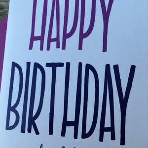May include: A white card with the text "Happy Birthday douchebag" in purple and blue lettering.