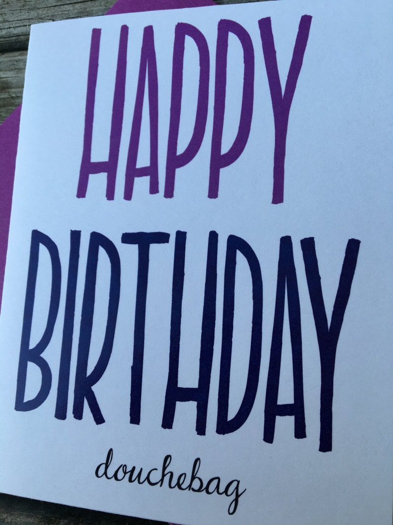 May include: A white card with the text "Happy Birthday douchebag" in purple and blue lettering.