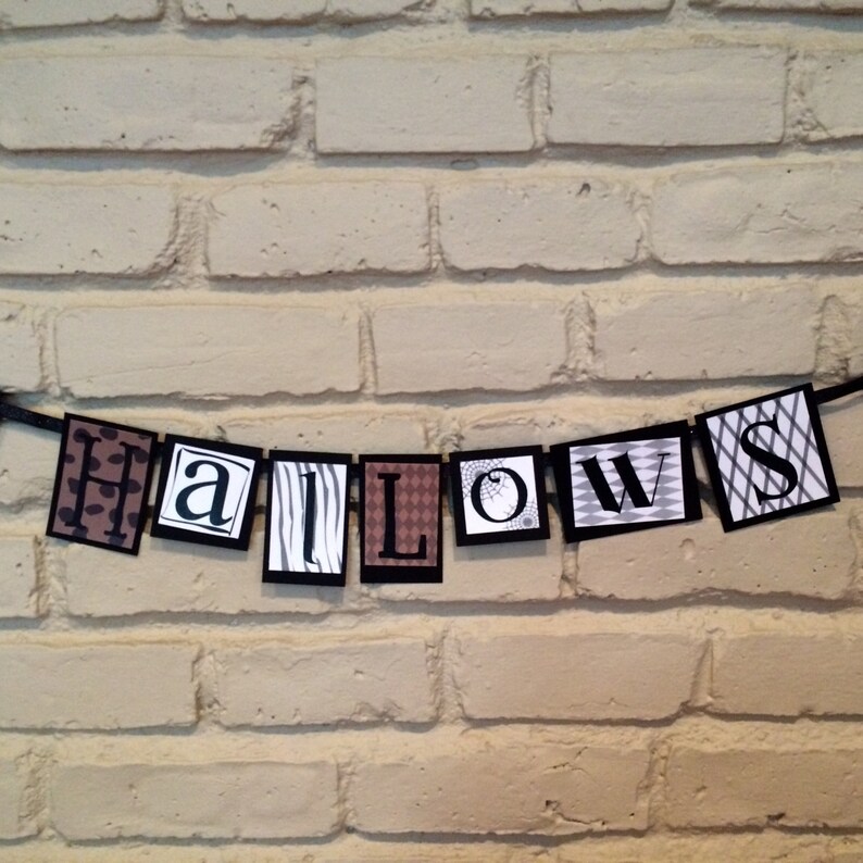 Pu&ograve; includere: Striscione di Halloween bianco e nero con la parola "HALLOWS" in lettere nere su sfondo bianco. Ogni lettera &egrave; su una carta con motivi diversi.