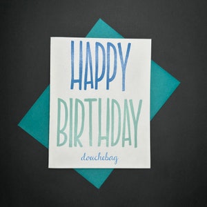 May include: A white card with blue and green text that says "Happy Birthday douchebag". The card is on a teal blue background.