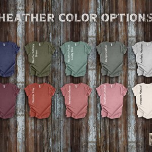 May include: Ten different colors of heather t-shirts with ruffled edges. The colors are: Heather Navy, Heather Military Green, Heather Prism Dusty Blue, Deep Heather, Athletic Heather, Heather Maroon, Heather Clay, Heather Mauve, Heather Orchid, and Heather Natural.