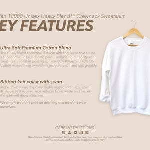 May include: A plain white Gildan crewneck sweatshirt on a wooden hanger. The sweatshirt has a ribbed knit collar and is made from a soft cotton blend. The image includes text detailing key features and care instructions.