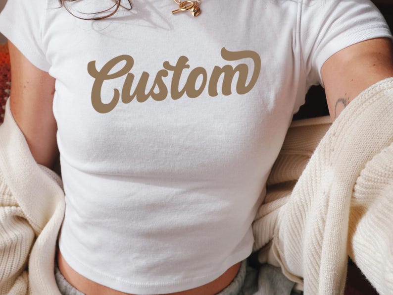 May include: White crop top with a brown "Custom" graphic in a retro font.