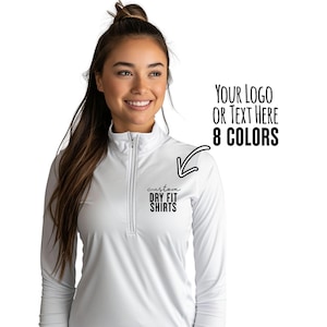 May include: A white long-sleeved dry-fit shirt with a quarter-zip collar. The shirt features the text "custom DRY FIT SHIRTS" on the chest. The image also includes the text "YOUR LOGO OR TEXT HERE 8 COLORS".