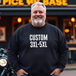 May include: A black sweatshirt with the text "CUSTOM 3XL-5XL" in white. The sweatshirt is worn by a person standing in front of a restaurant. A motorcycle is visible in the background.