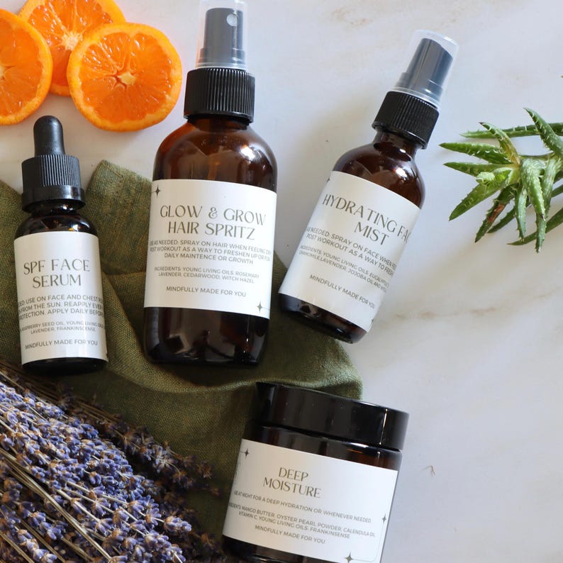 K&ouml;nnte beinhalten: Eine Auswahl an Hautpflegeprodukten in braunen Glasflaschen und -gl&auml;sern, darunter ein Serum, Haarspray, Gesichtsspray und eine Feuchtigkeitscreme. Die Produkte sind mit Orangenscheiben, Lavendel und Gr&uuml;nzeug auf einer wei&szlig;en Oberfl&auml;che angeordnet.