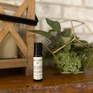 May include: A black roller bottle with a white label that reads "Grounded AF" and includes the text "Deep Root Connection, Meditation & for Daily Grounding/Support, Young Living Oils Thoughtfully Mixed with Oil, Truly Made for You".