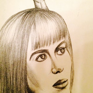 May include: Pencil sketch portrait of a person with long hair and a guitar headstock atop their head. The drawing is in shades of gray and black, with detailed shading on the face and hair.