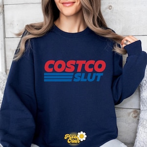 Op de afbeelding: Marineblauwe sweatshirt met de tekst "COSTCO SLUT" in rood en blauw, die het logo van een bekend merk imiteert. De tekst is vetgedrukt. De sweatshirt heeft een ronde hals en lange mouwen.