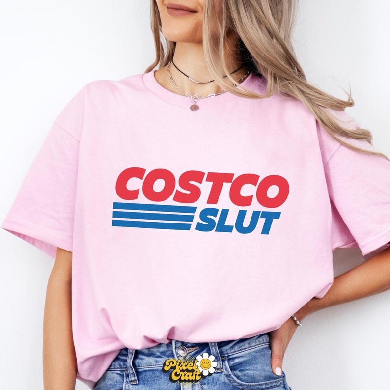 Op de afbeelding: Lichtroze t-shirt met de tekst "COSTCO SLUT" in rood en blauw. De tekst is vetgedrukt en zonder schreef. Het t-shirt heeft een ronde hals en korte mouwen.