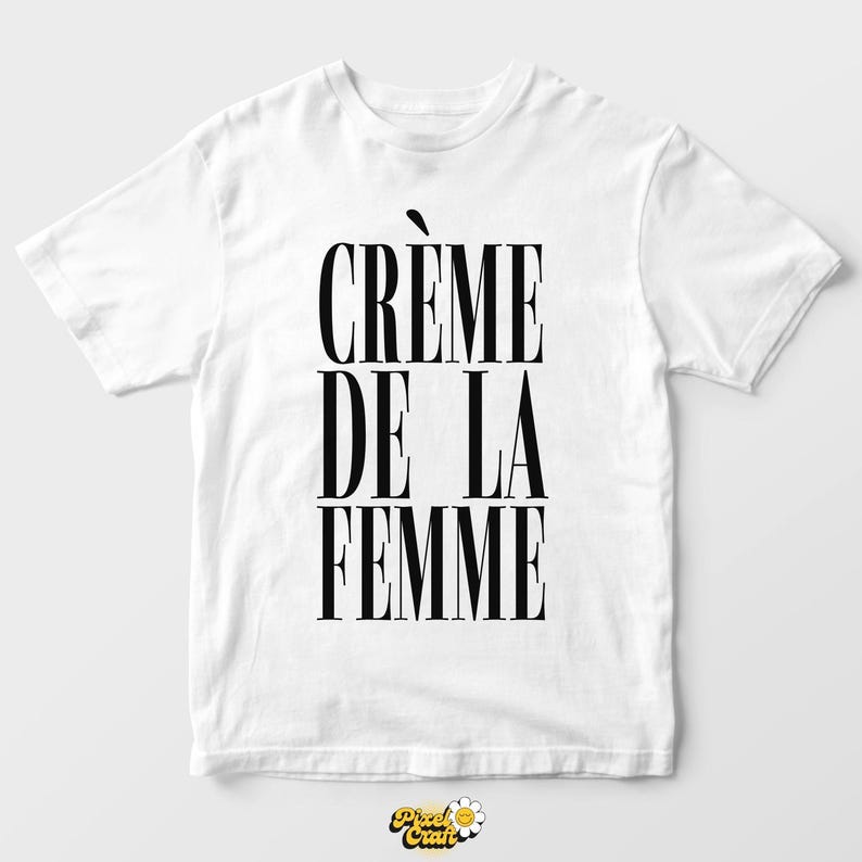 May include: White t-shirt with the text "CR&Egrave;ME DE LA FEMME" in bold, black capital letters. The text is vertically stacked. The shirt has short sleeves and a crew neck.