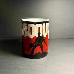 Puede incluir: Una taza de cerámica blanca con la silueta negra de una persona sosteniendo una motosierra sobre un fondo rojo. La palabra GROOVY está impresa en letras mayúsculas blancas grandes y desgastadas en la parte superior del diseño.