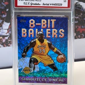 May include: A graded 2025 Topps NBA trading card featuring Shaquille O'Neal in a Los Angeles Lakers uniform. The card is part of the 8-Bit Ballers series and is graded GEM MINT 10. The card is encased in a protective holder.