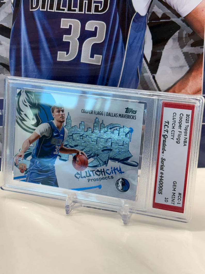 May include: A basketball card featuring Cooper Flagg of the Dallas Mavericks, encased for protection. The card displays the text "CLUTCHCITY Prospects" and the Topps logo. It is graded GEM MINT 10.