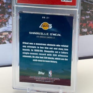 May include: A basketball card featuring Shaquille O'Neal of the Lakers, displayed in a protective case. The card's reverse side details O'Neal's accomplishments, including a record of 336 offensive rebounds in the 1999/00 season.
