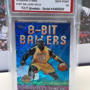 May include: A 2025 Topps NBA trading card of Shaquille O'Neal, part of the 8-Bit Ballers HOLO series. The card shows O'Neal in a yellow Lakers uniform, holding a basketball. It's graded GEM MINT 10 and encased in a protective holder.