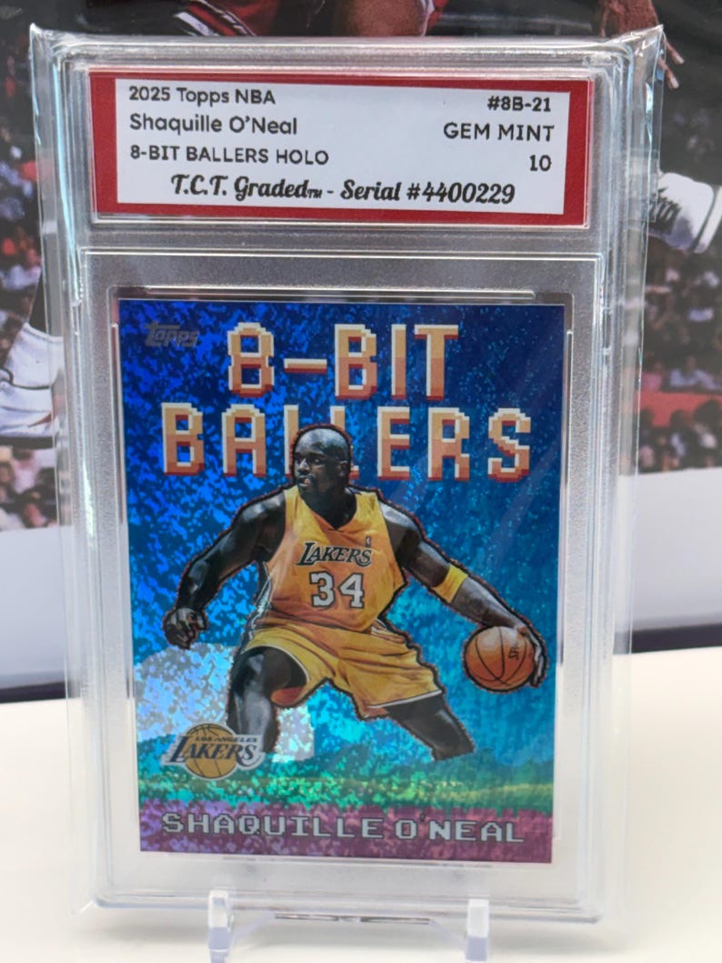 May include: A 2025 Topps NBA trading card of Shaquille O'Neal, part of the 8-Bit Ballers HOLO series. The card shows O'Neal in a yellow Lakers uniform, holding a basketball. It's graded GEM MINT 10 and encased in a protective holder.