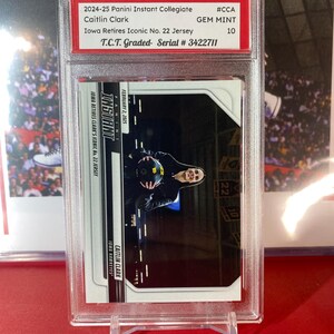 May include: A graded trading card of Caitlin Clark, a basketball player for the Iowa Hawkeyes. The card is from the 2024-25 Panini Instant Collegiate series and is graded GEM MINT 10 by T.C.T. The card features a photo of Clark holding a basketball in a black and white photo. The card is numbered 3422711.