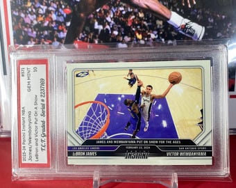 Op de afbeelding: Een basketbal trading card met LeBron James en Victor Wembanyama, beiden in hun teamtruien, tijdens een wedstrijd. De kaart is uit de 2023-24 Panini Instant NBA-serie en is beoordeeld als GEM MINT 10. De kaart heeft serienummer #2237169.