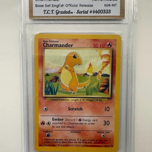 May include: A graded 1999 Pokémon Charmander card in a protective case. The card features an orange lizard-like creature with a flame on its tail. The card is graded NM-MT and has the text "Base Set English Official Release".