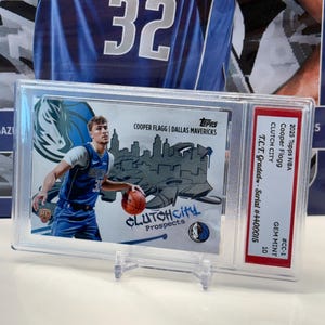 May include: A 2025 Topps NBA trading card featuring Cooper Flagg of the Dallas Mavericks, encased in a protective holder. The card displays "CLUTCH CITY Prospects" text and is graded GEM MINT 10. The card is in a clear plastic case.