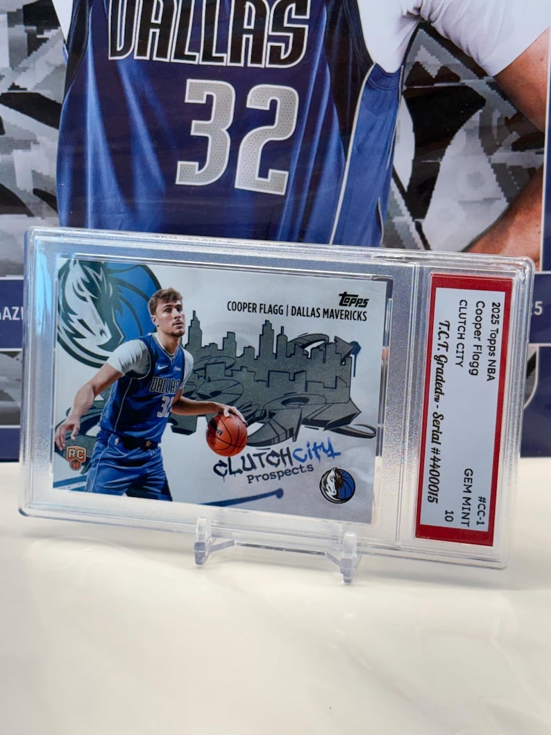 May include: A 2025 Topps NBA trading card featuring Cooper Flagg of the Dallas Mavericks, encased in a protective holder. The card displays "CLUTCH CITY Prospects" text and is graded GEM MINT 10. The card is in a clear plastic case.