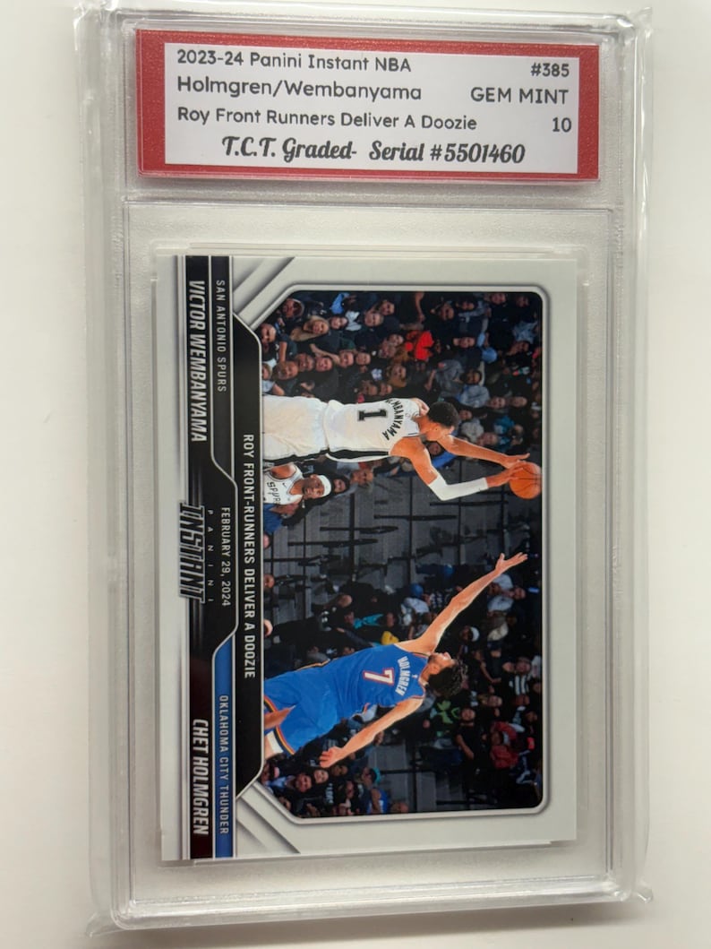 Op de afbeelding: Een Panini Instant NBA-verzamelkaart met Chet Holmgren en Victor Wembanyama. De kaart is beoordeeld met GEM MINT 10 door T.C.T. en bevat de tekst "Roy Front Runners Deliver A Doozie". De kaart zit in een beschermende houder.