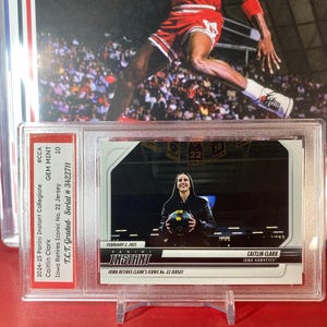 May include: A trading card featuring Caitlin Clark, a basketball player for the Iowa Hawkeyes. The card is from the 2024-25 Panini Instant Collegiate series and is graded GEM MINT 10 by T.C.T. The card features a photo of Clark holding a basketball and the text "Iowa Retires Clark's Iconic No. 22 Jersey".
