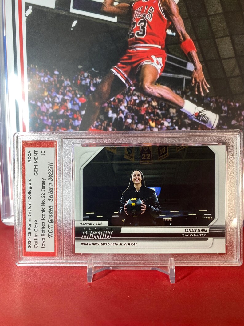 May include: A trading card featuring Caitlin Clark, a basketball player for the Iowa Hawkeyes. The card is from the 2024-25 Panini Instant Collegiate series and is graded GEM MINT 10 by T.C.T. The card features a photo of Clark holding a basketball and the text "Iowa Retires Clark's Iconic No. 22 Jersey".