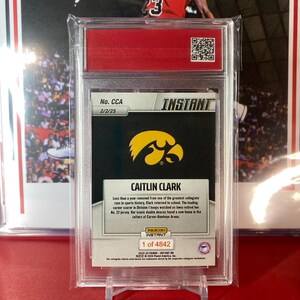 May include: A trading card featuring Caitlin Clark, a basketball player for the University of Iowa. The card is silver with a black background and features a photo of Clark in her Iowa uniform. The card is numbered 2/2/25 and is part of the Instant set. The card also includes a quote from Clark about her return to school after a successful collegiate career.