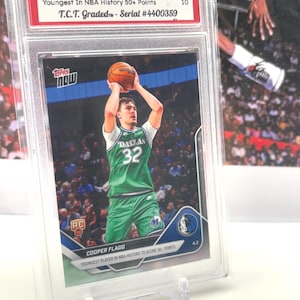 May include: A graded Cooper Flagg basketball card from the 2026 Topps Now NBA series. The card features a player in a green Dallas Mavericks uniform shooting a basketball. The card is graded GEM MINT 10 by T.C.T. and is serial numbered #4400359.