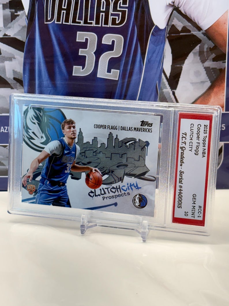 May include: A basketball card featuring Cooper Flagg of the Dallas Mavericks, encased for protection. The card displays the text "CLUTCHCity Prospects" and the team logo. It is graded GEM MINT 10.