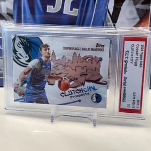 May include: A basketball card featuring Cooper Flagg of the Dallas Mavericks, encased for protection. The card displays the team logo and the text "CLUTCH City Prospects." It is graded and has a serial number.