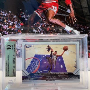 May include: A graded basketball card featuring LeBron James and Victor Wembanyama. The card is encased in a protective holder and graded a 10. The card's text reads "JAMES AND WEMBANYAMA PUT ON SHOW FOR THE AGES" and "INSTANT". A background image of Michael Jordan is visible.