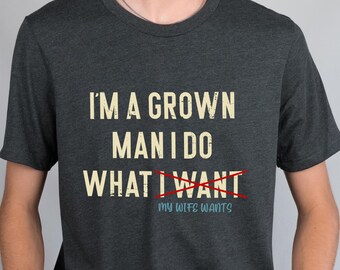 May include: A dark gray t-shirt with the text "I'm a grown man I do what I want" with the word "want" crossed out and the text "My wife wants" underneath.
