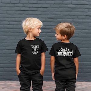 May include: Two children wearing black t-shirts with white text and graphics. The shirt on the left says "TOBY" and has a badge with the words "Ring Security". The shirt on the right says "Ring Security" with the date "08-06-2024" and the words "Johnson Wedding".