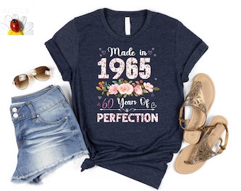 Puede incluir: Una camiseta azul marino con un diseño floral y el texto "Made in 1965 60 Years of Perfection".