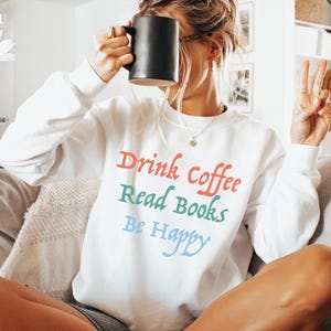 May include: White sweatshirt with the text "Drink Coffee Read Books Be Happy" in colourful lettering.