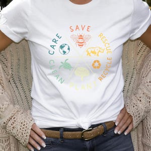 Puede incluir: Camiseta blanca con un dise&ntilde;o gr&aacute;fico colorido que presenta un c&iacute;rculo con las palabras "Save", "Care", "Clean", "Plant", "Rescue" y "Recycle" alrededor. El gr&aacute;fico tambi&eacute;n incluye im&aacute;genes de una abeja, una tortuga, un &aacute;rbol, un rinoceronte y un globo terr&aacute;queo.