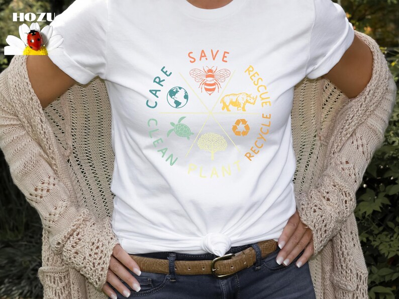 Puede incluir: Camiseta blanca con un dise&ntilde;o gr&aacute;fico colorido que presenta un c&iacute;rculo con las palabras "Save", "Care", "Clean", "Plant", "Rescue" y "Recycle" alrededor. El gr&aacute;fico tambi&eacute;n incluye im&aacute;genes de una abeja, una tortuga, un &aacute;rbol, un rinoceronte y un globo terr&aacute;queo.