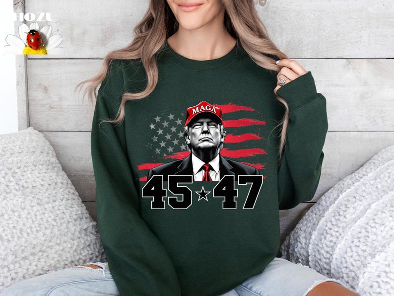 Puede incluir: Sudadera verde oscuro con un gr&aacute;fico de un hombre con una gorra roja "MAGA", sobre un fondo de bandera estadounidense estilizada. Los n&uacute;meros "45" y "47" est&aacute;n debajo, en negrita.