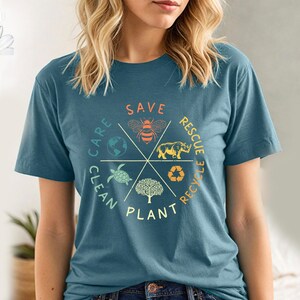 Puede incluir: Una camiseta azul turquesa con un dise&ntilde;o gr&aacute;fico circular que presenta una abeja, un rinoceronte, una tortuga, un &aacute;rbol y un globo terr&aacute;queo. El gr&aacute;fico tiene las palabras "Save, Rescue, Recycle, Plant, Clean, Care" alrededor del c&iacute;rculo.