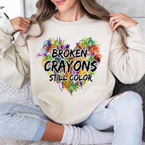 May include: A cream colored sweatshirt with a colorful heart design and the text "Broken Crayons Still Color".