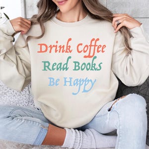 May include: A beige sweatshirt with the text "Drink Coffee Read Books Be Happy" in colourful lettering.