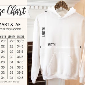 Puede incluir: Una sudadera con capucha blanca Smart & AF Heavy Blend en una percha, con una tabla de tallas que muestra las medidas en pulgadas. La tabla incluye tallas de la S a la 5XL, detallando las medidas de ancho, largo y manga para cada talla. La sudadera tiene un bolsillo delantero y una capucha.