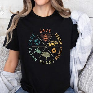 Puede incluir: Camiseta negra con un dise&ntilde;o gr&aacute;fico circular que presenta las palabras "Save, Plant, Clean, Care, Rescue, Recycle" en un estilo vintage. El gr&aacute;fico tambi&eacute;n incluye una abeja, una tortuga, un rinoceronte, un &aacute;rbol y un globo terr&aacute;queo.